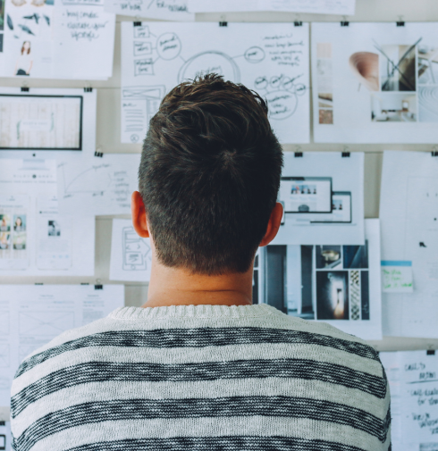 A founder studying sketches and plans pinned to a wall